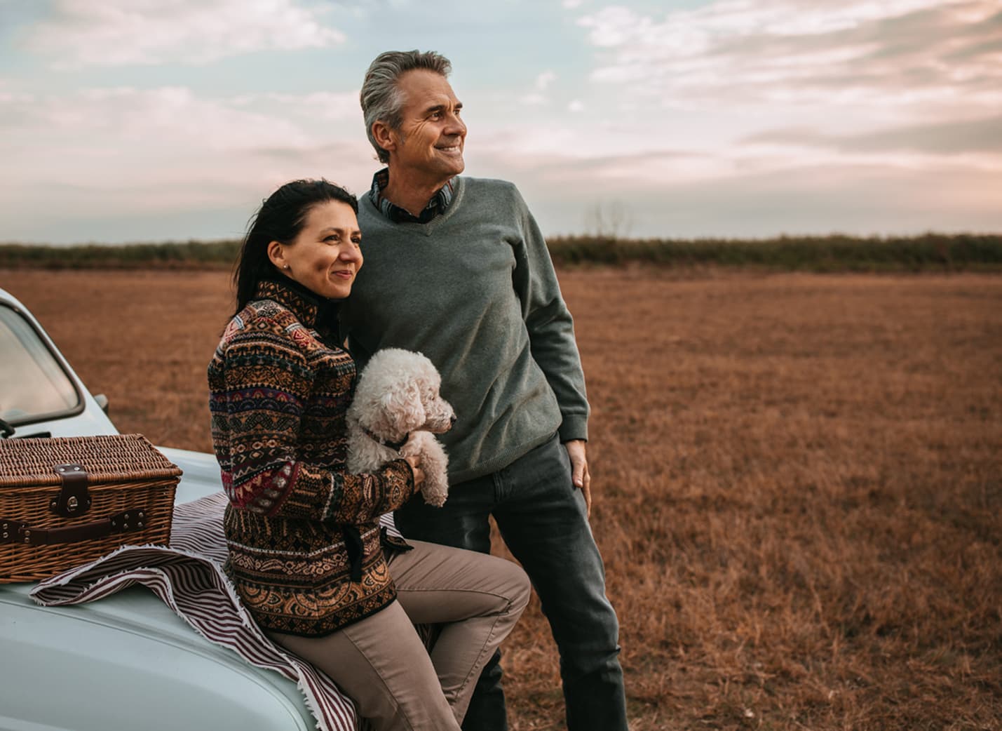A couple looking at the horizon in a field, with a small dog.